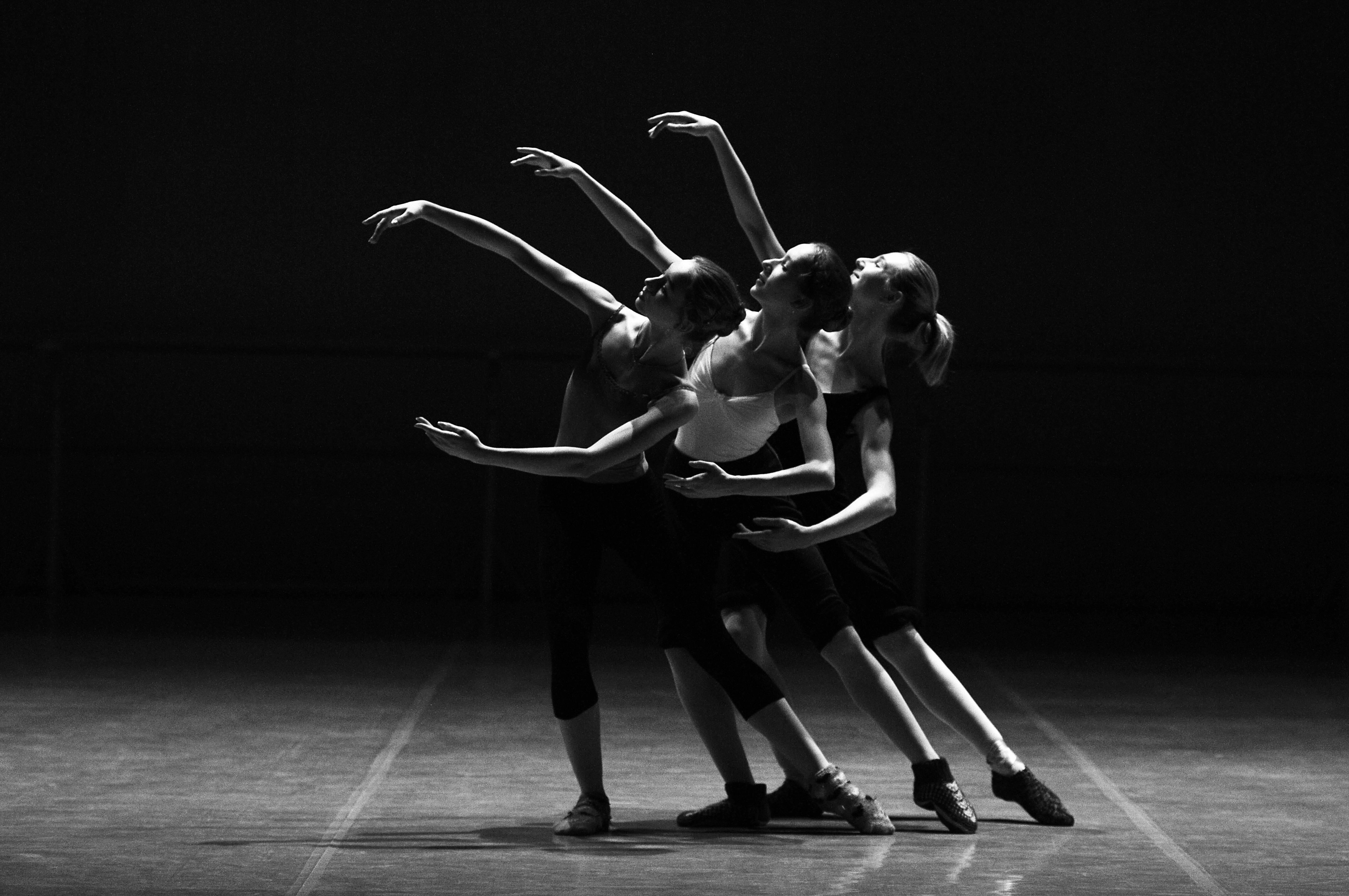 Three female ballerinas perform a synchronized dance on stage in dramatic lighting.